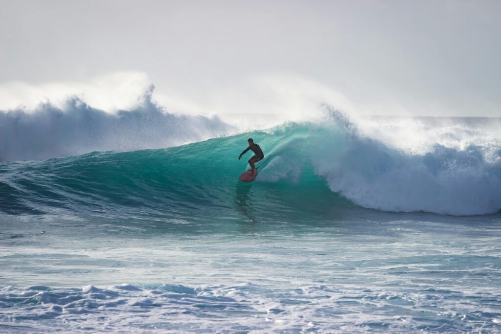 Surfer skillfully riding a massive ocean wave under clear daylight.
